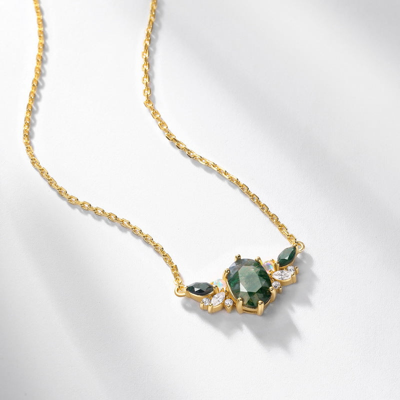 Gold necklace: Oval moss agate pendant with green gemstone, opal, and crystal details, on a white surface.