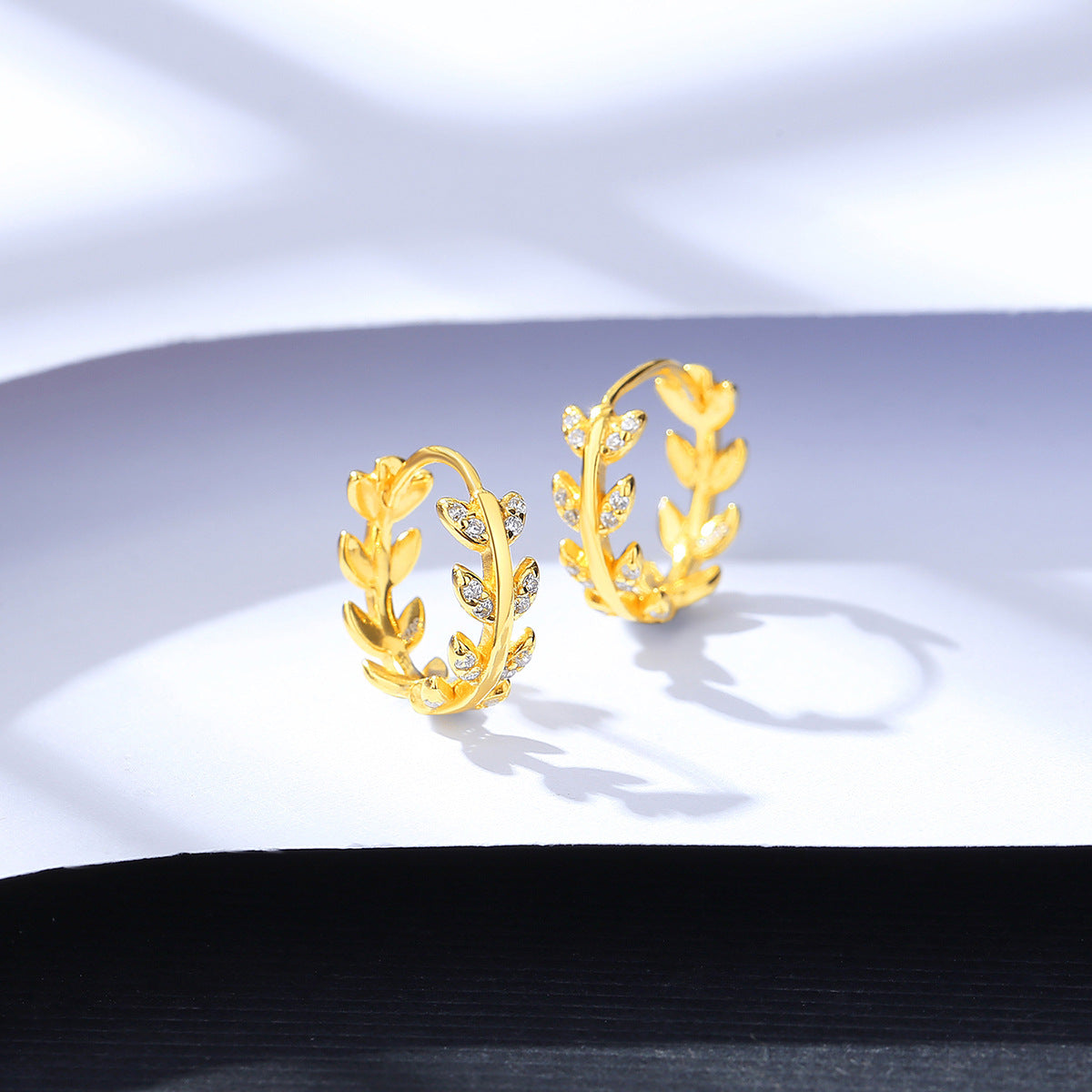 Gold hoop earrings with leaf design on a white background