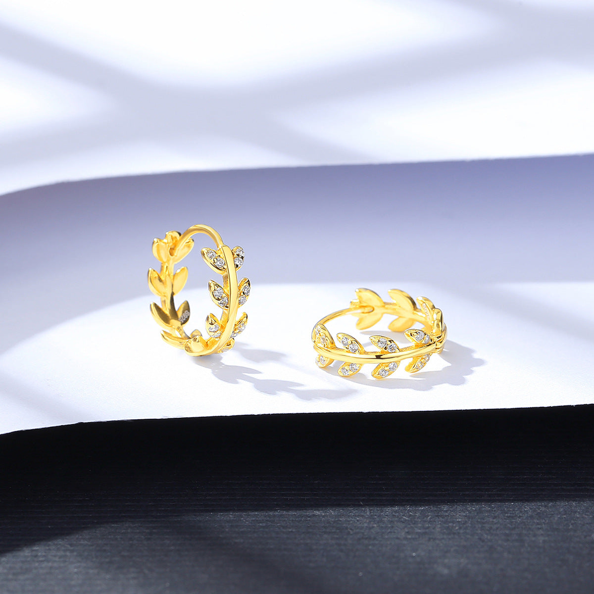 Two gold hoop earrings on a white fabric background