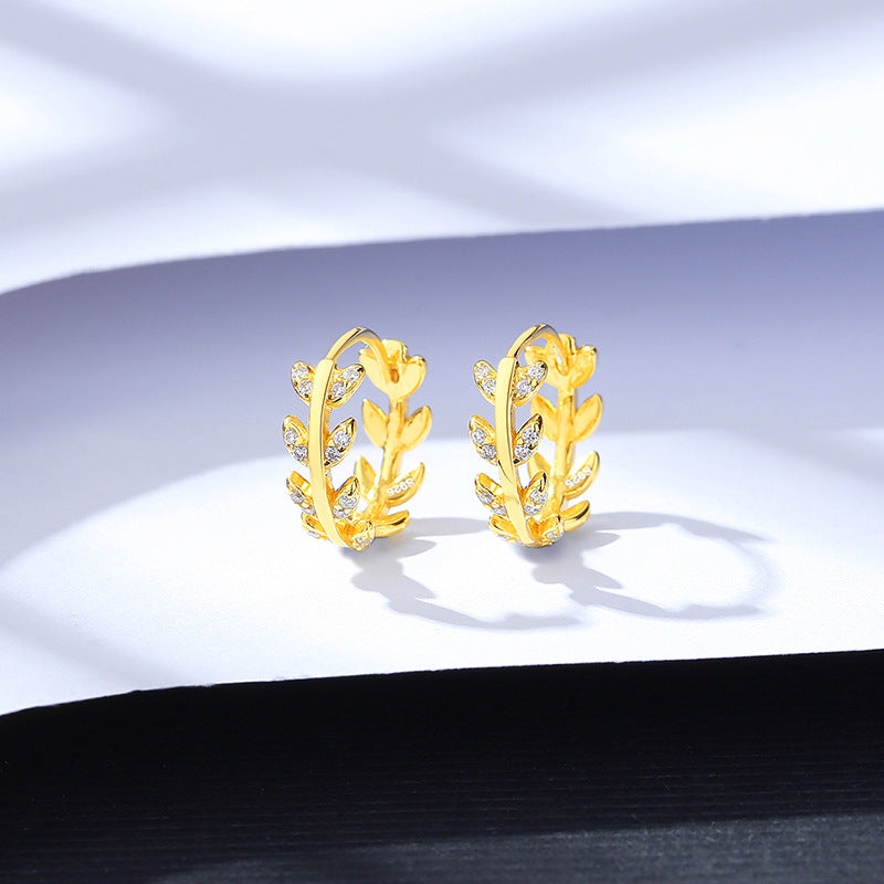 Gold earrings with leaf design on a white fabric background