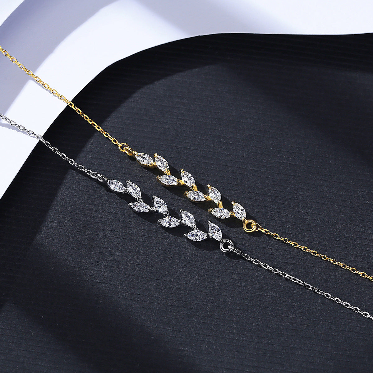 Two gold and silver necklaces with leaf-like design on a dark surface