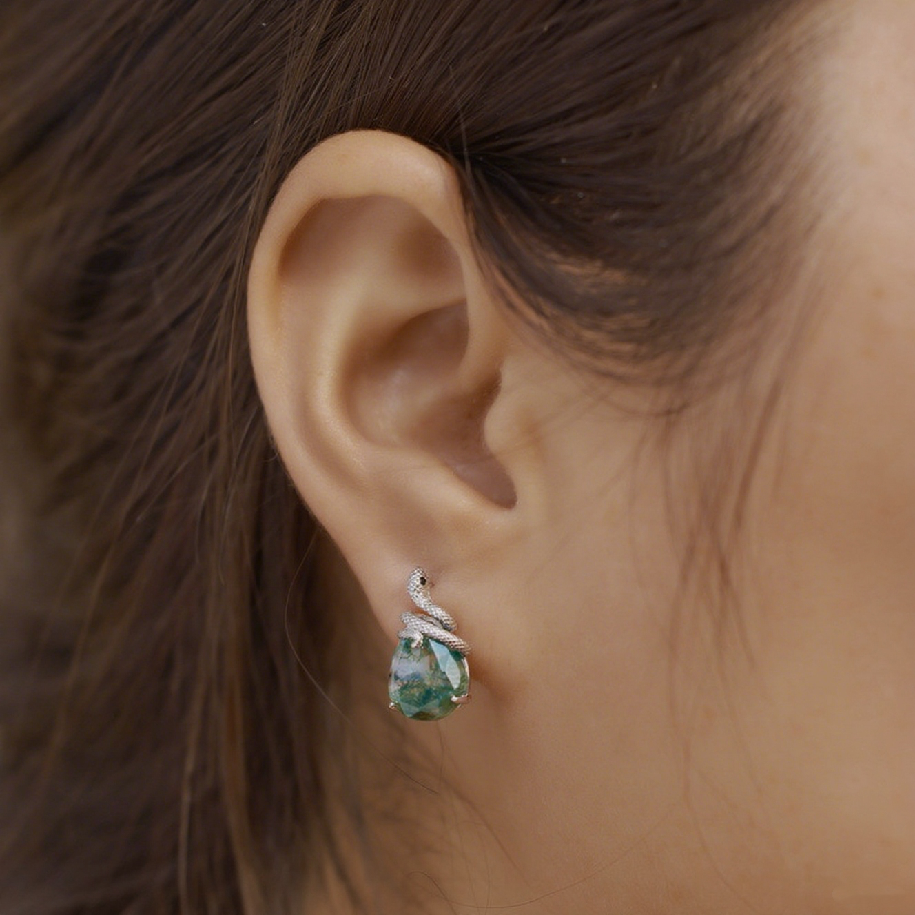 Close - up of silver - toned earring on a person: Snake - wrapped teardrop moss agate, showcasing the intricate design.